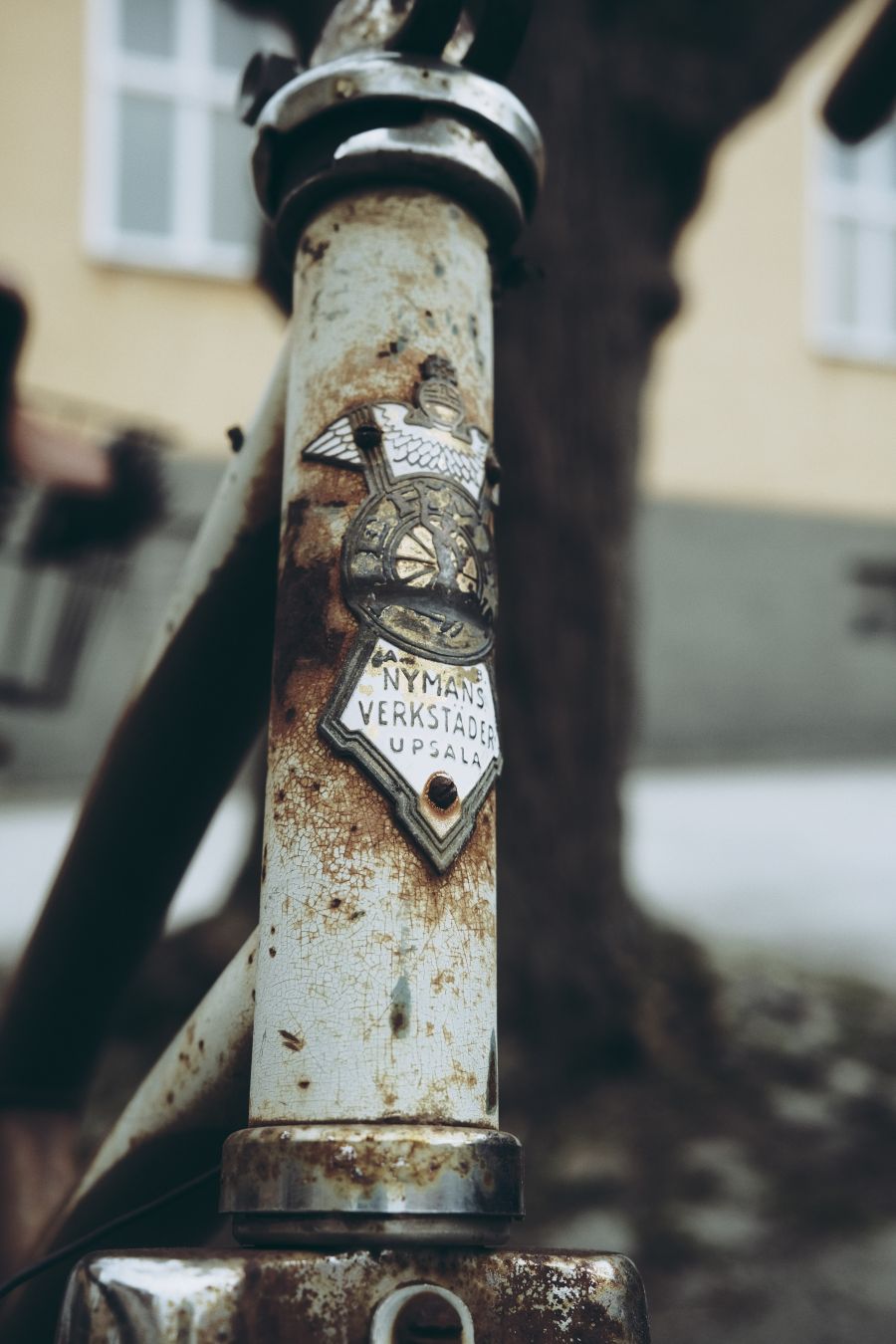 Närbild på emblemet på en gammal rostig cykel. Texten lyder 'Nymans verkstäder Uppsala'.