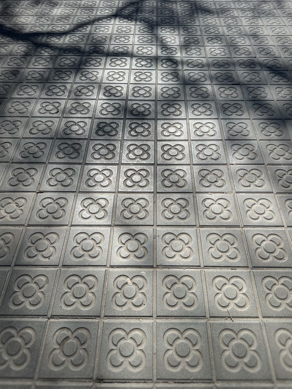 Concrete pavers with a very classical flower pattern from a sidewalk in Barcelona. There is a pronounced tree shadow coming in from the top left.