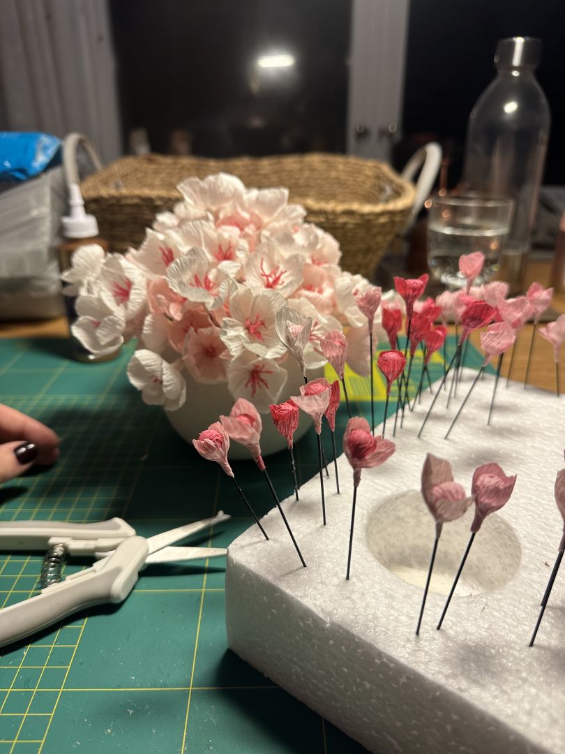 A vase with pink and white flowers and a number of pink buds, all made out of paper