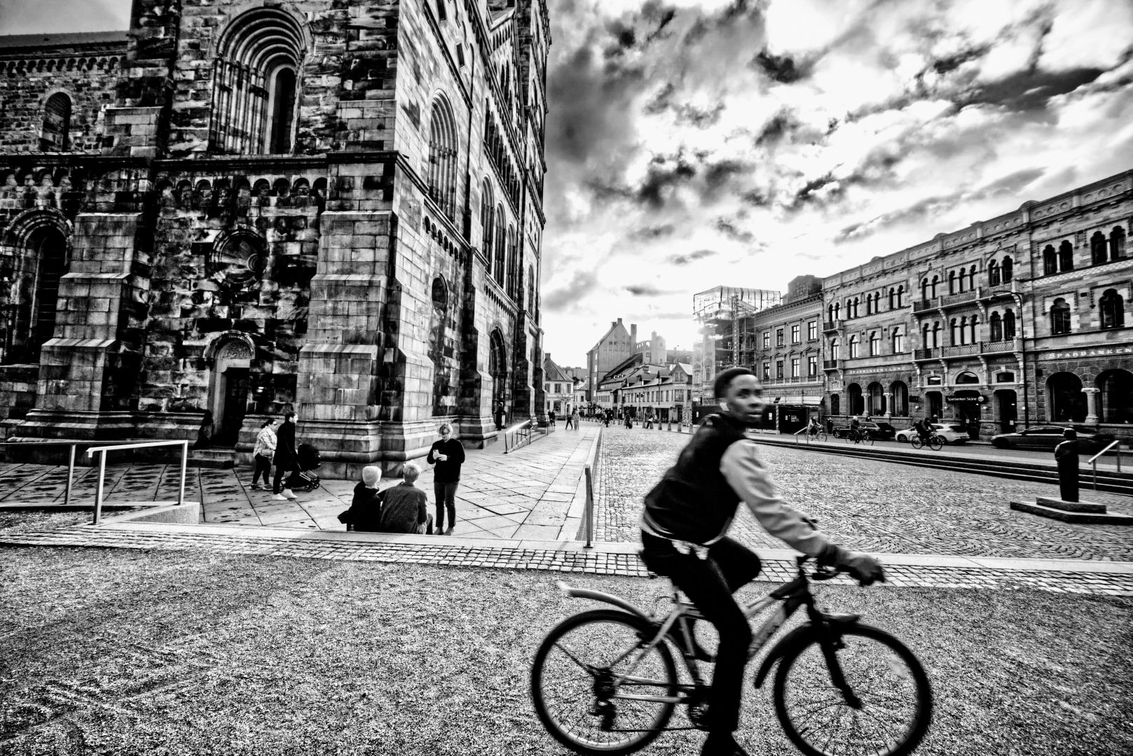 En cyklist i Lundagård framför Lunds domkyrka. Svartvitt, motljus.