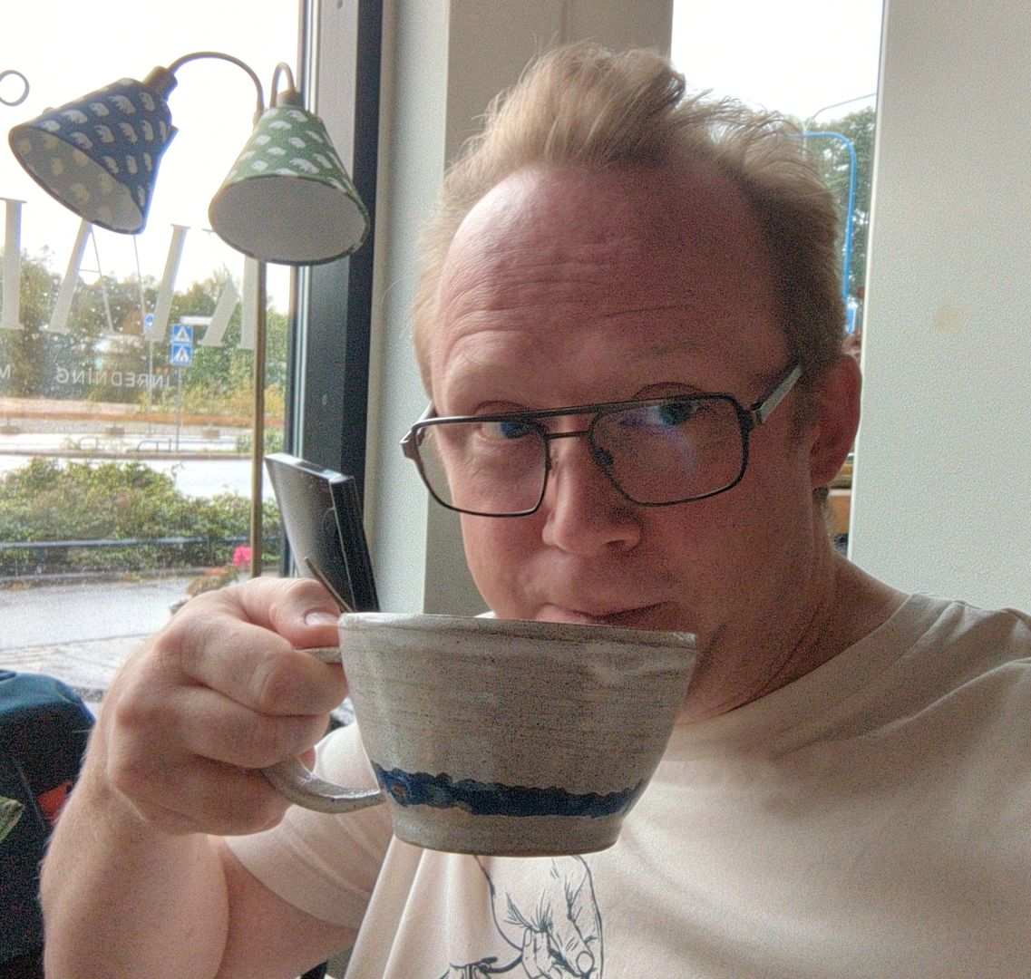 Selfie där jag sitter på kafé och sörplar te ur en låg, vid mugg. I bakgrunden syns ett fönster där det står en golvlampa.