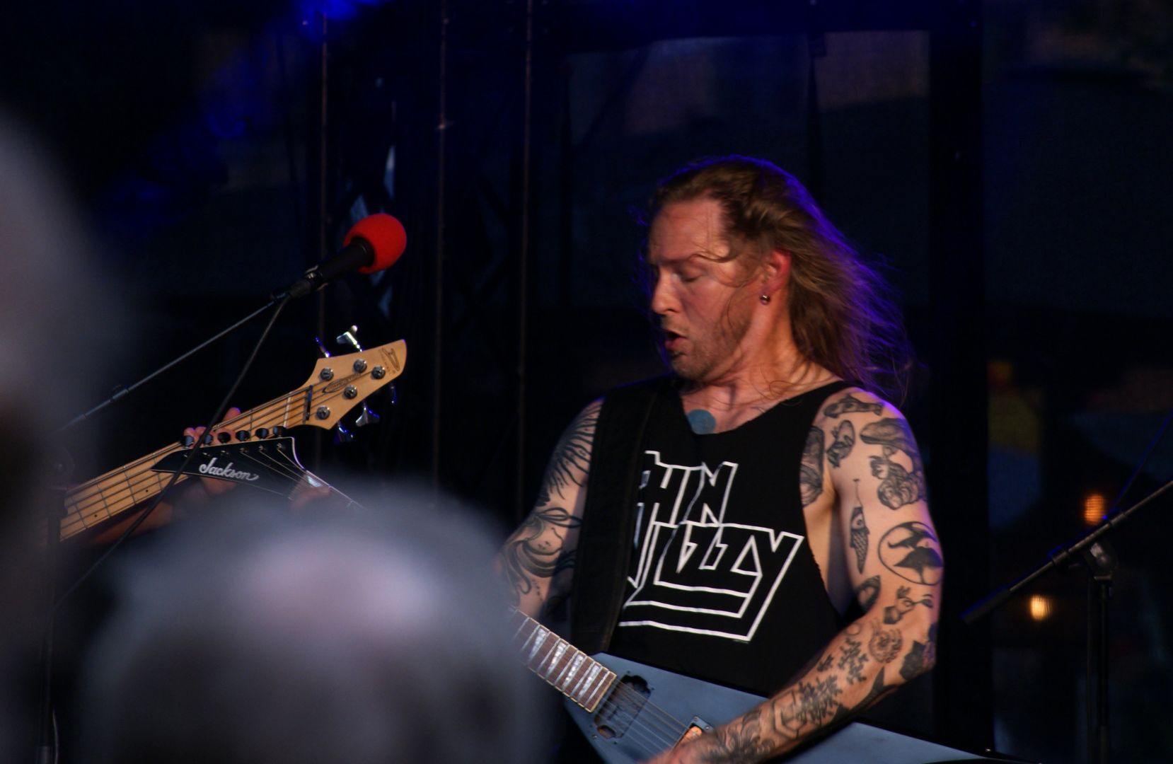 Sångaren fotad från midjan och uppåt. Han är starkt fokuserad på sitt gitarrspel och står lätt tilbakalutad med munnen halvöppen och blicken riktad ned mot gitarren. Håret flyger bakom honom.