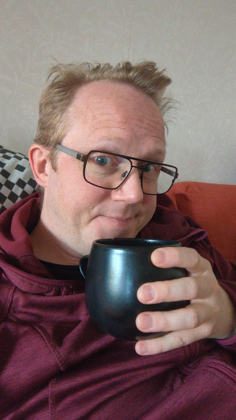 Selfie i soffan tagen i halvprofil. Jag håller en stor svart mugg framför mig, stödd mot bröstet och tittar in k kameran. Jag ler med halva munnen och ger kameran en tveksam blick.