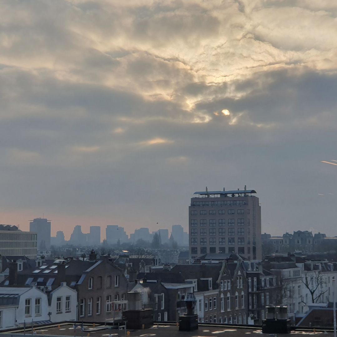 A skyline of Amsterdam from a high building. Dramatic sky with the sun almost peeking through.